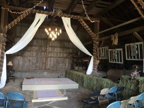 Hay bales, lights, drapery, and custom mason jar and crystal wagon wheel chandeliers made this wedding ceremony country chic. 