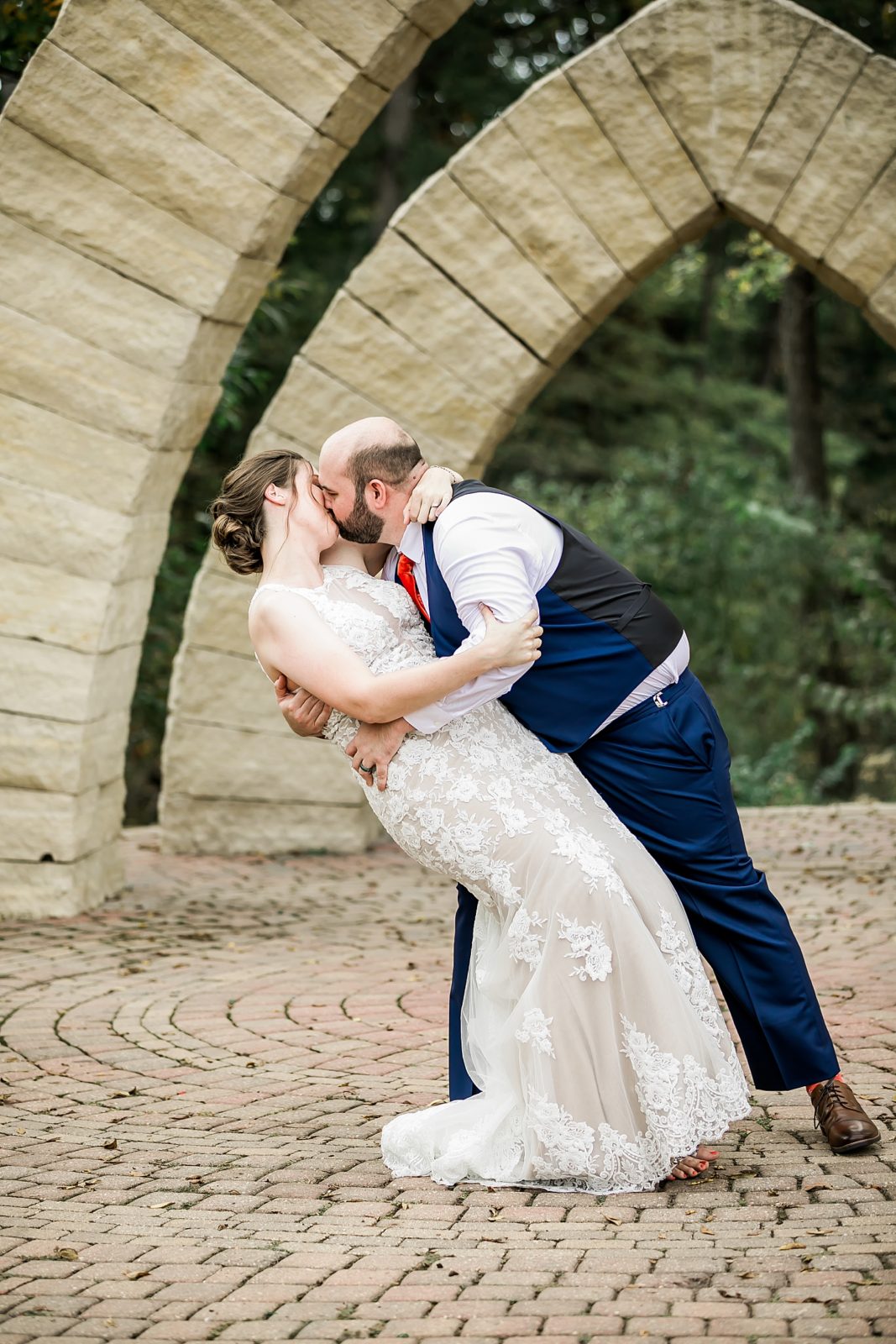 bride and groom kiss under stone arches at celebration farms in iowa city