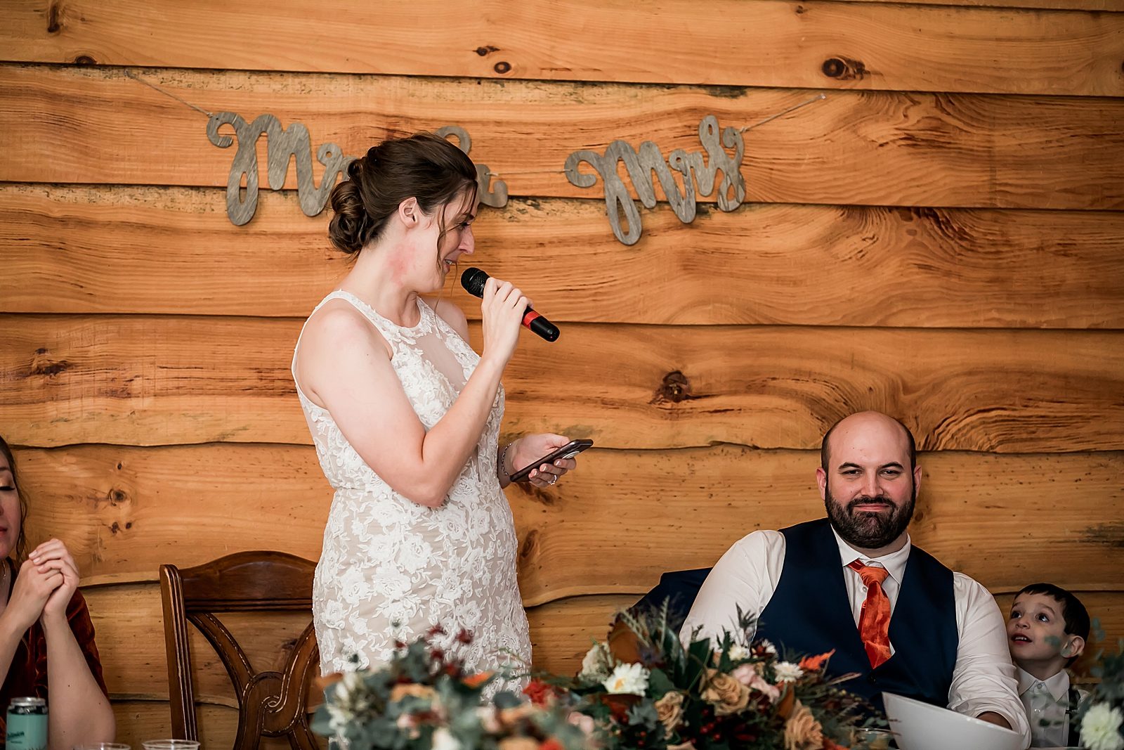 bride gives speech at wedding reception while looking at groom