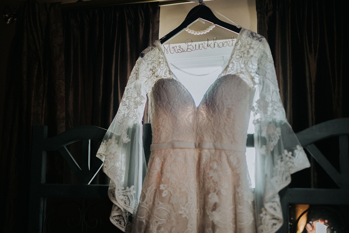 wedding dress with lace sleeves hanging in front of window