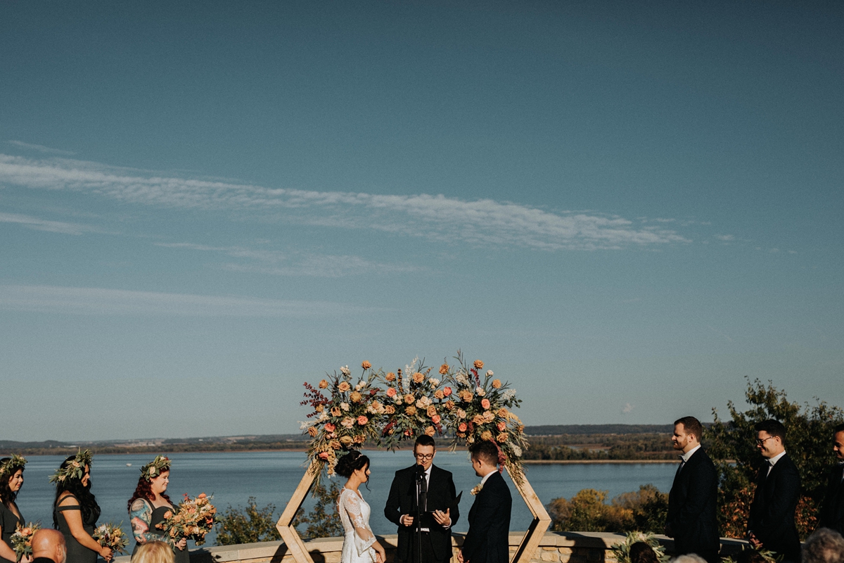 bride and groom under wooden floral hexagon arch overlooking water