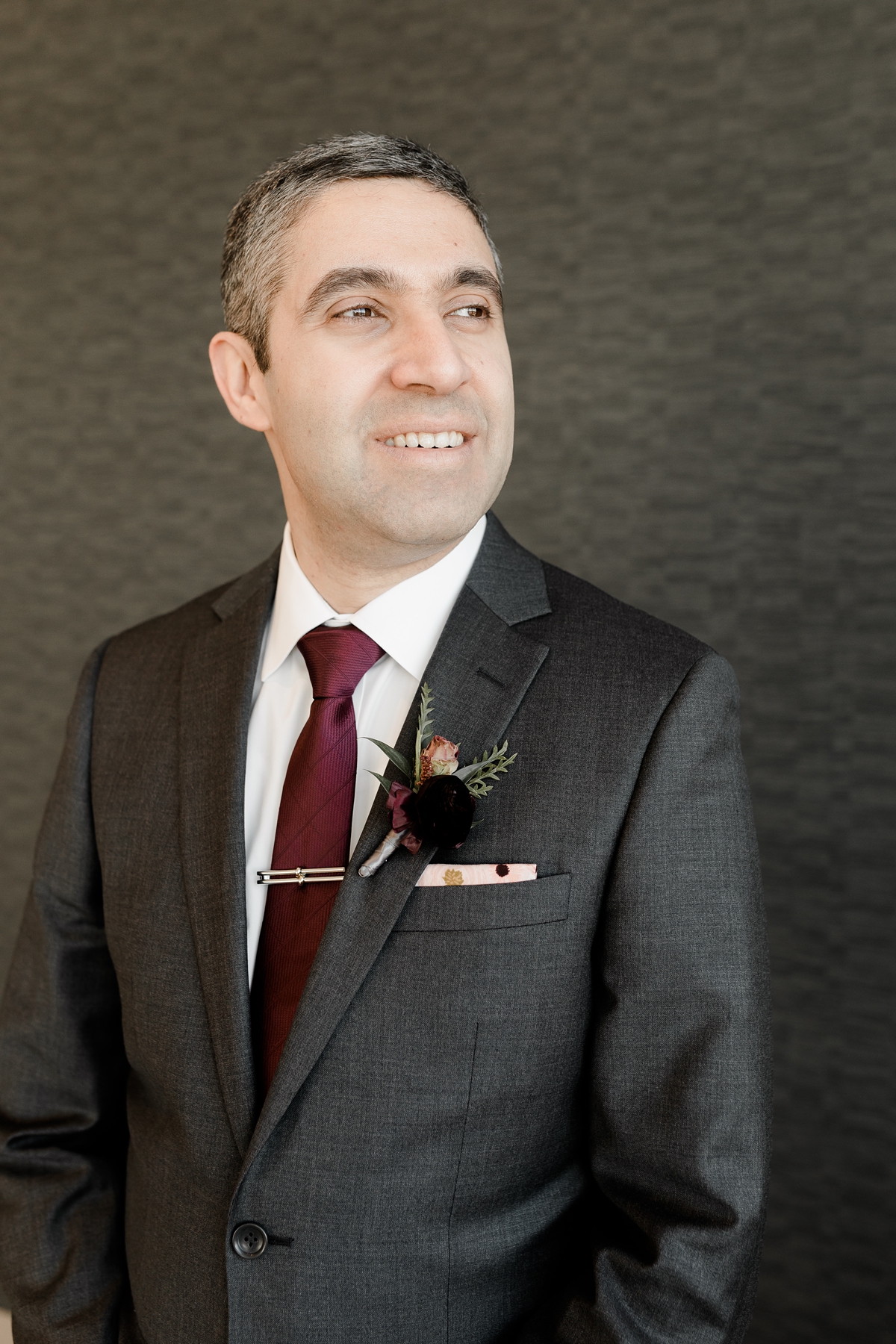 Groom grey suit with maroon and pink boutonnière and tie