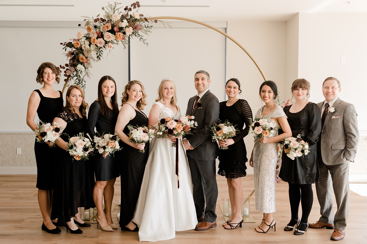 bridal party standing under floral gold metal wedding arch