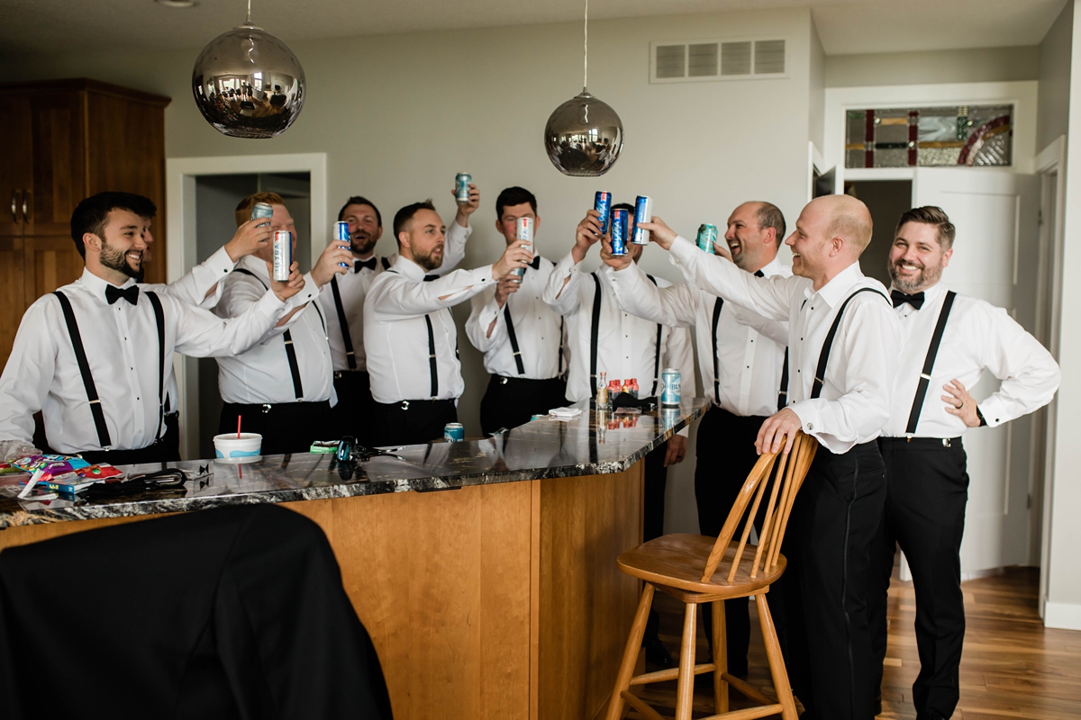 Groomsmen cheersing groom with beers while getting ready.