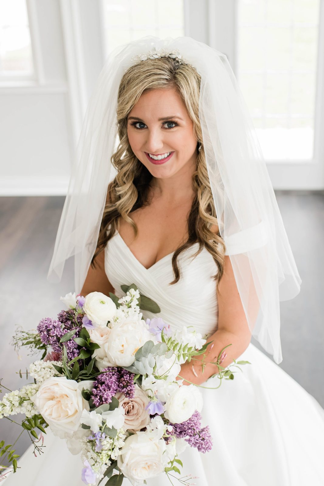 Bride smiling with purple and white wedding bouquet.