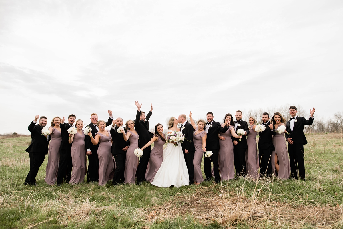 Bridal party cheering on couple while they kiss.