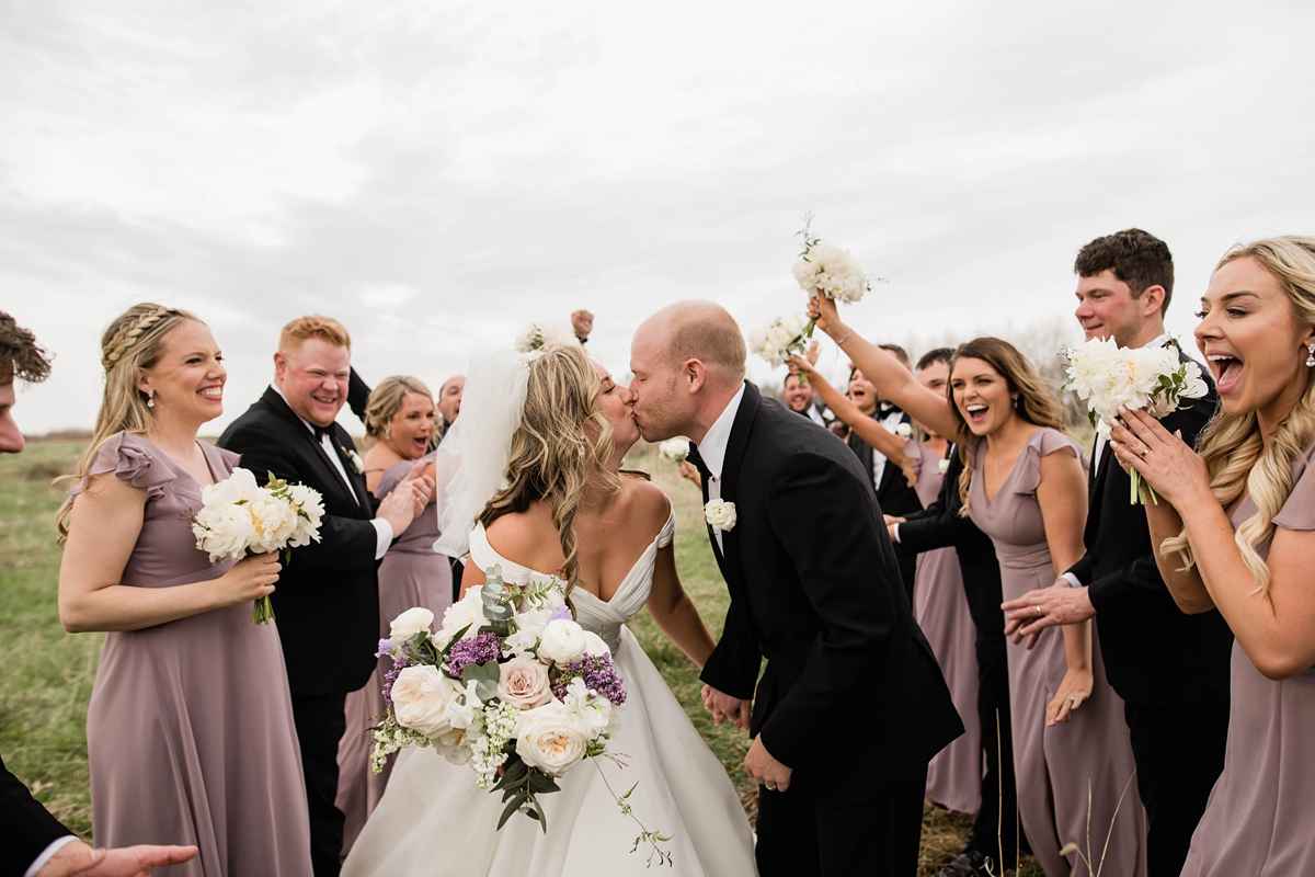 Bride and groom kissing while bridal party cheers.