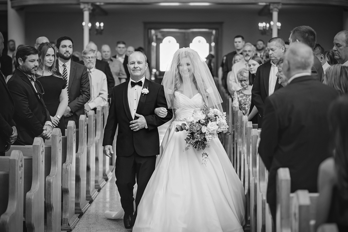 Black and white image of bride being walked down the aisle by her father.