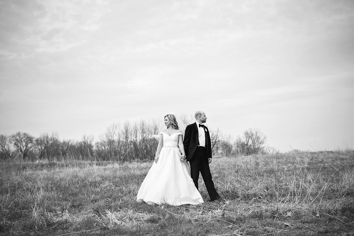 Black and white of bride and groom standing in field.