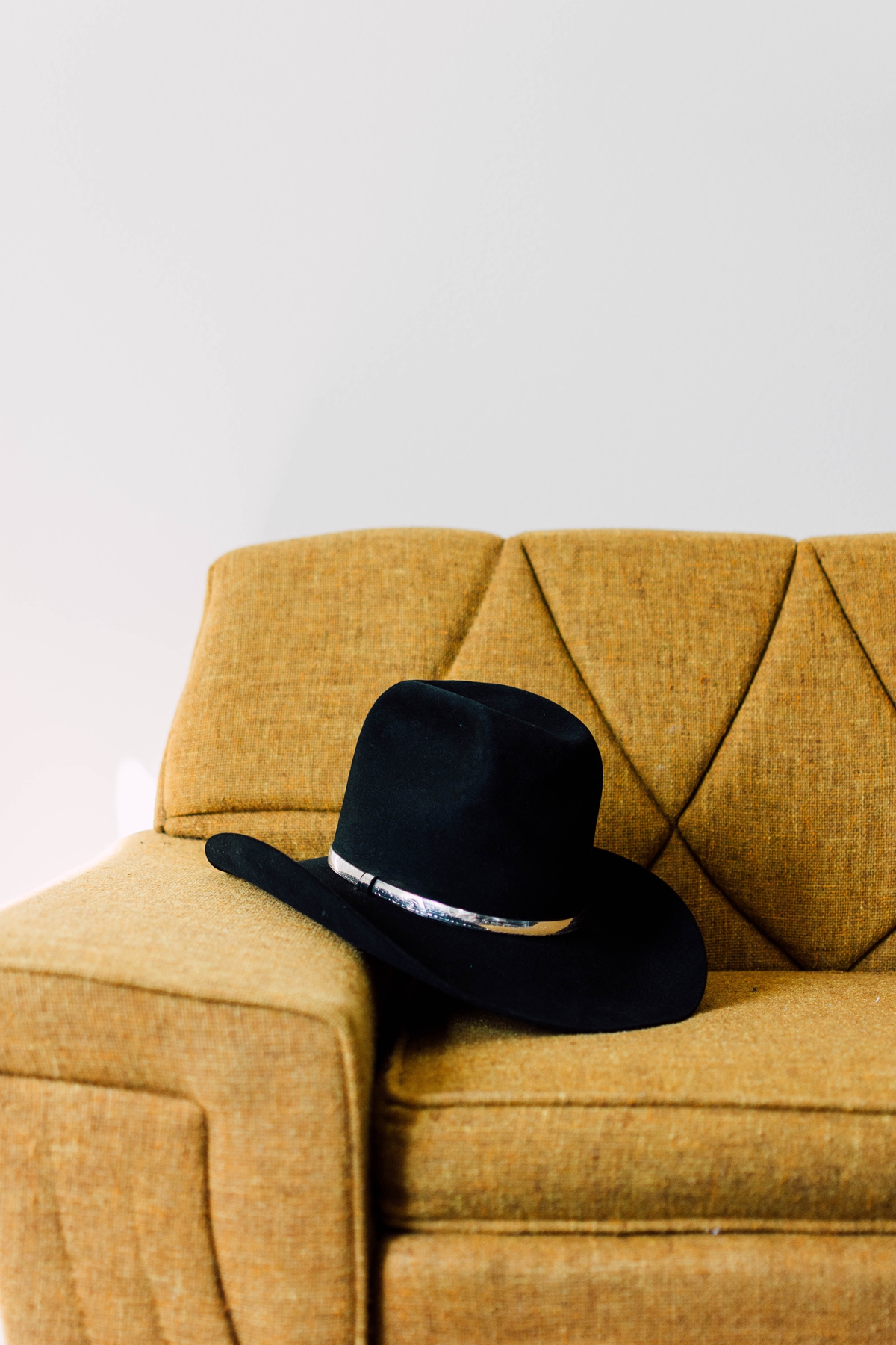 Gathering Barn Williamsburg Iowa Wedding black groom's cowboy hat on yellow couch