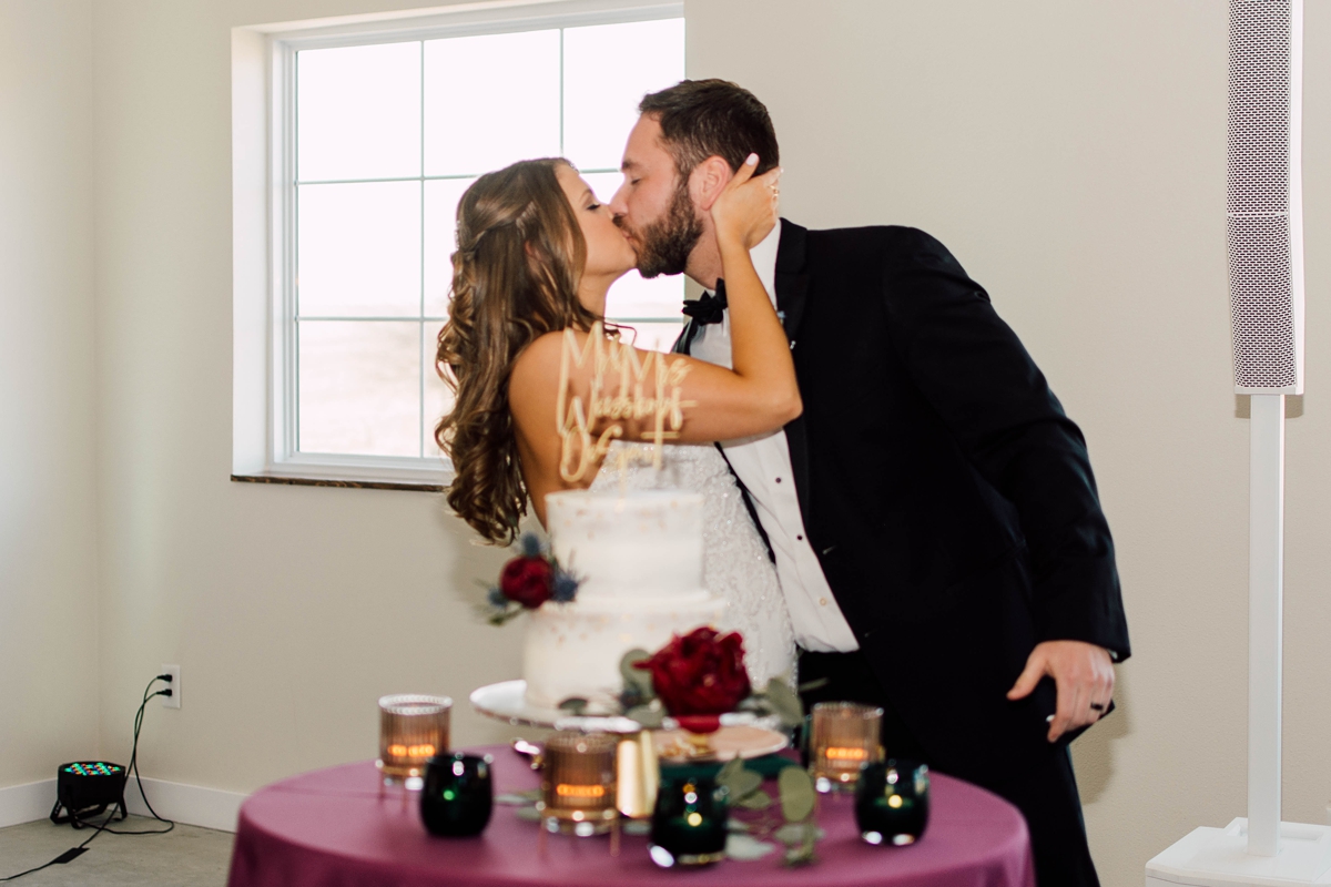 Gathering Barn Williamsburg Iowa Wedding bride and groom kiss after cutting cake