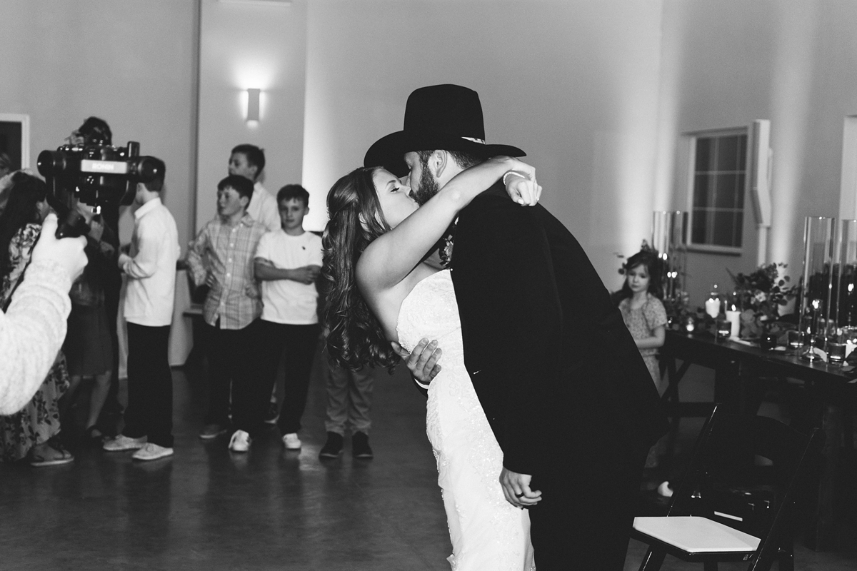 Gathering Barn Williamsburg Iowa Wedding bride and groom in cowboy hat kiss while dancing at reception