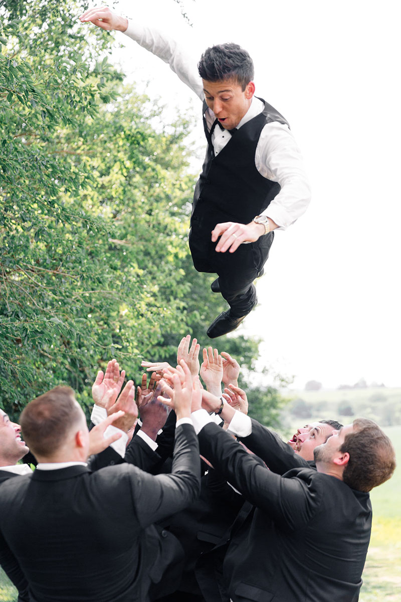 Groom is flying in the air during photos with groomsmen