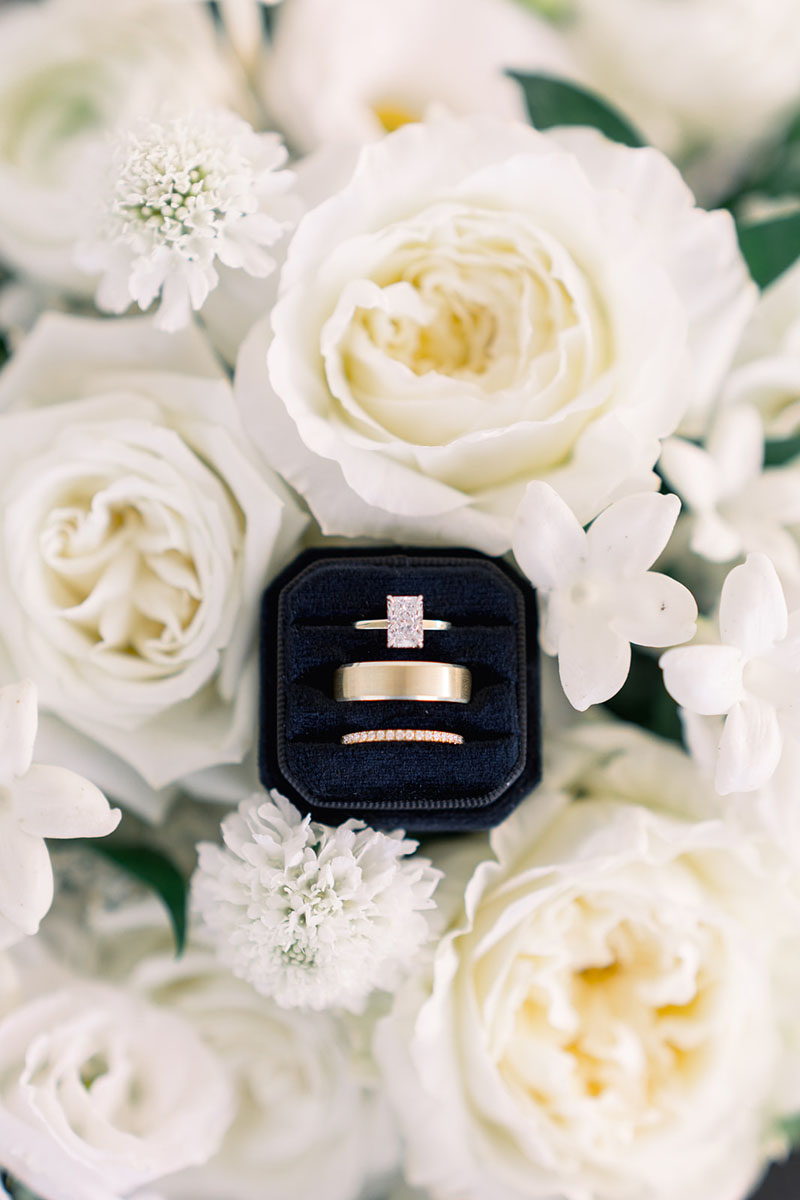 black ring box with large diamond engagement ring and wedding bands in flowers